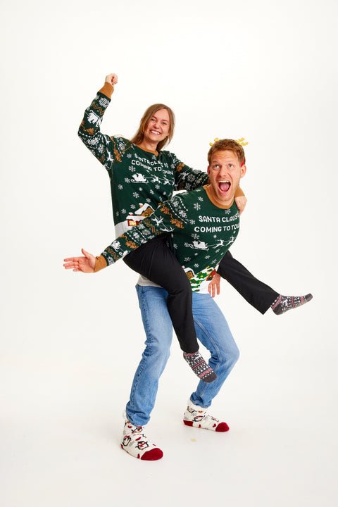 En kvinde der sidder på ryggen af en mand, hvor de begge er iført samme grønne julesweater.