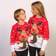 En børn kigger på hinanden og poserer sammen i røde julesweatre med snefnug og rensdyr på.