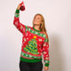 En dame poserer med en julekugle og er iført en julesweater med et juletræ på.