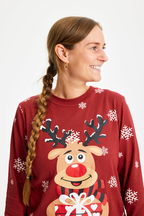 En smilende dame kigger til siden og er iført røde julepyjamas med Rudolf på.
