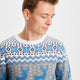 En mand kigger ned og er iført en blå julesweater med mønster på.