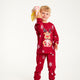 Et barn med en gave I hånden iført røde julepyjamas med Rudolf på.