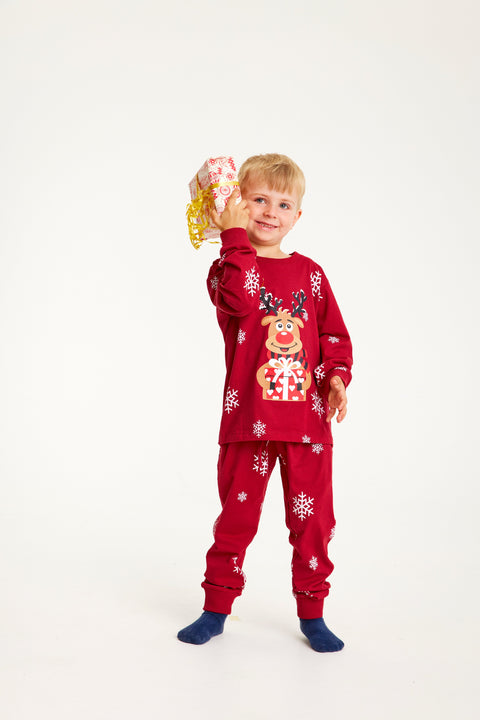 Et barn med en gave I hånden iført røde julepyjamas med Rudolf på.